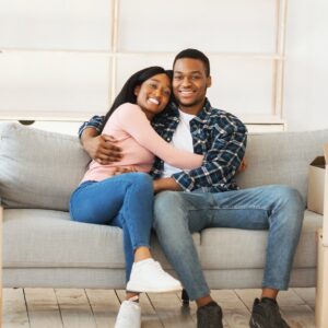 Positive black couple resting on sofa on moving day at their new home, panorama