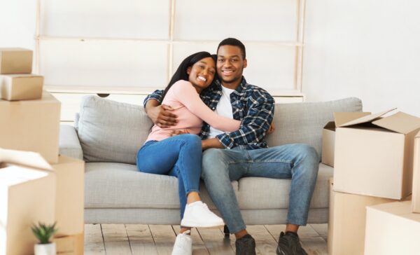 Positive black couple resting on sofa on moving day at their new home, panorama